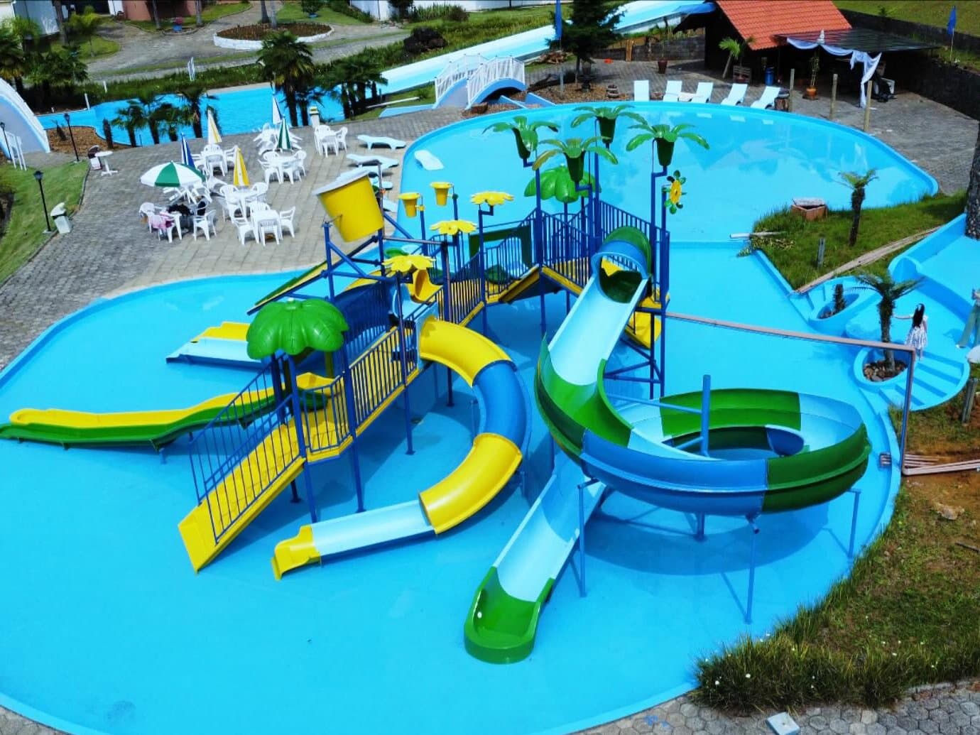 Brinquedo aquático infantil com escorregadores amarelos, verdes e azuis sobre a piscina rasa, visto do alto