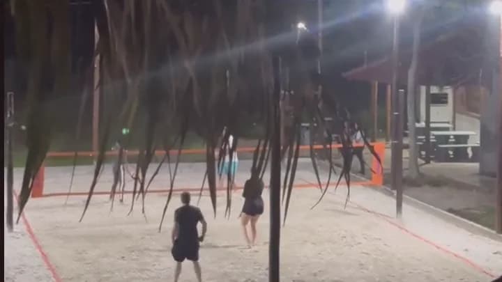 Quadra de beach tennis iluminada à noite, com jogadores ao longe