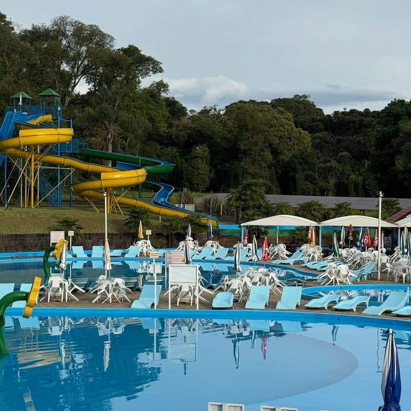 Piscina com espreguiçadeiras e guarda-sóis, e toboáguas ao fundo