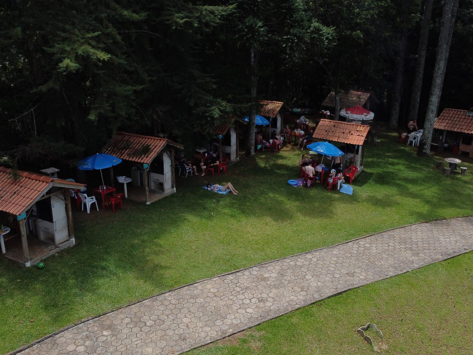 Quiosques com churrasqueira e mesas no gramado, à sombra das árvores